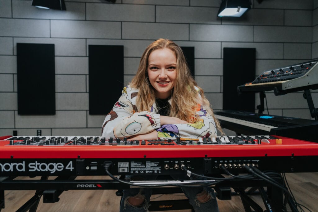 Woman with long blonde hair in cartoon character hoodie sitting with elbows on red keyboard.