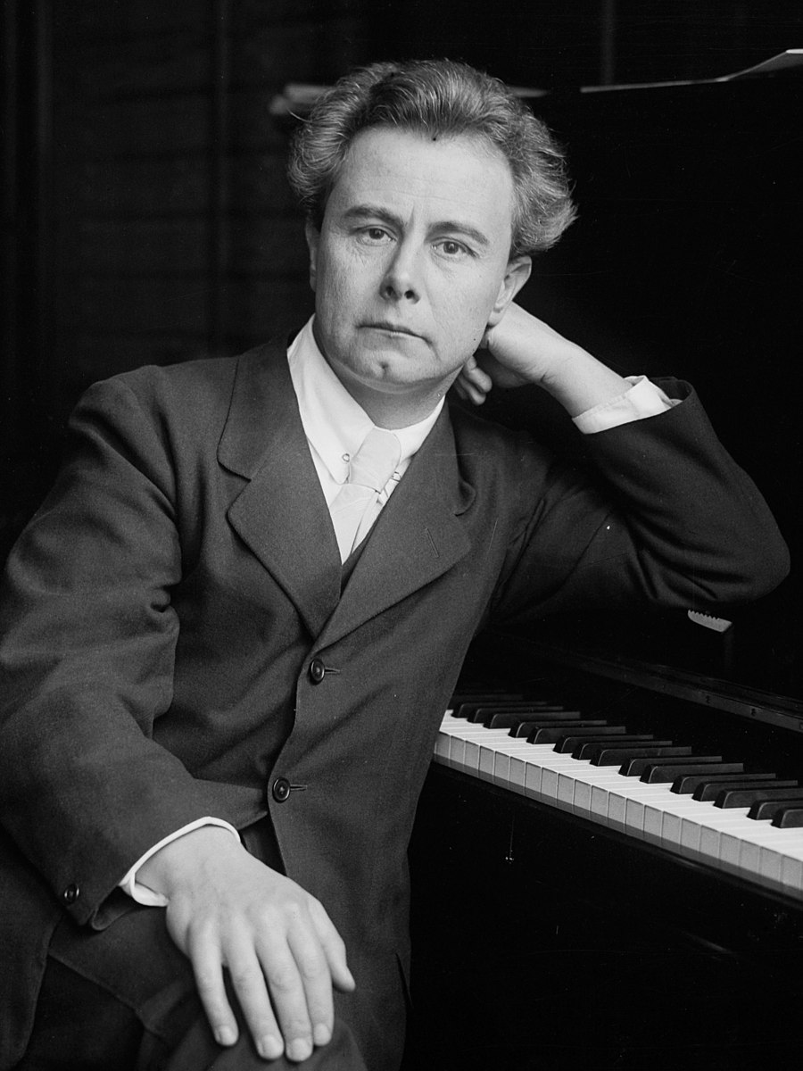 Man sitting leaning on piano in suit.
