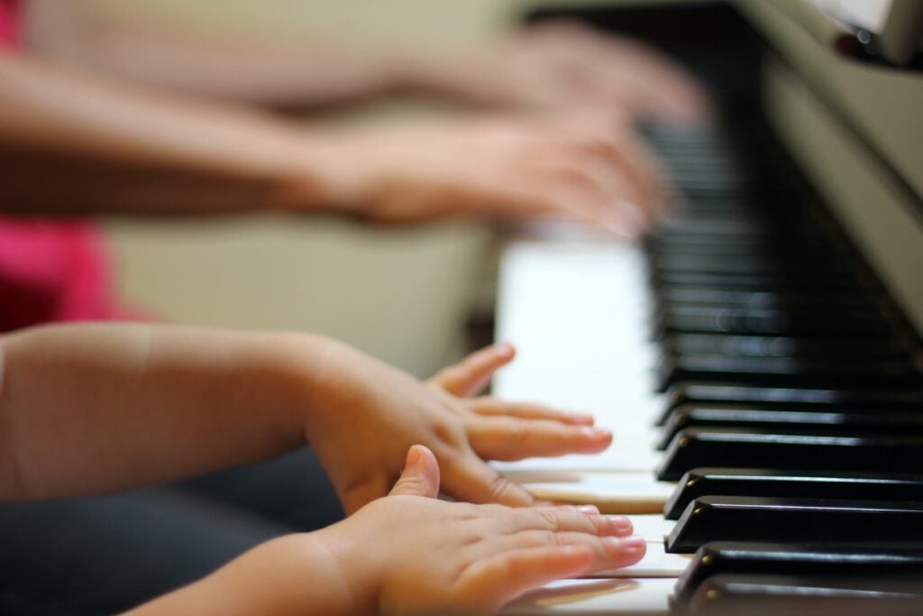 Small child hands on keyboard with adult hands in the background.